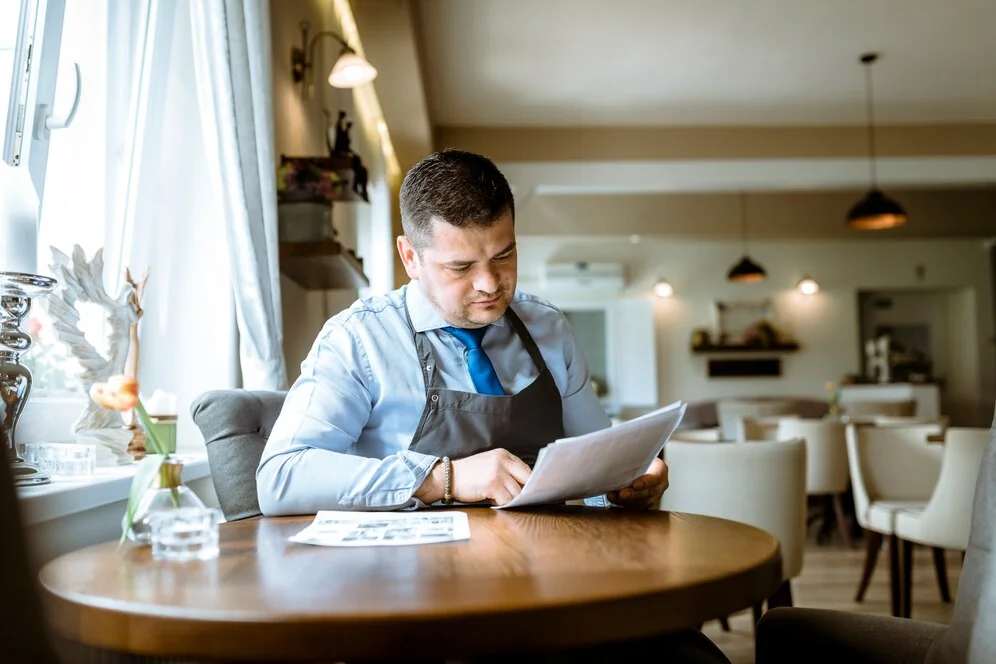 Restaurant manager reviewing ADA compliance paperwork, documenting paper trail for accessibility standards in the dining area