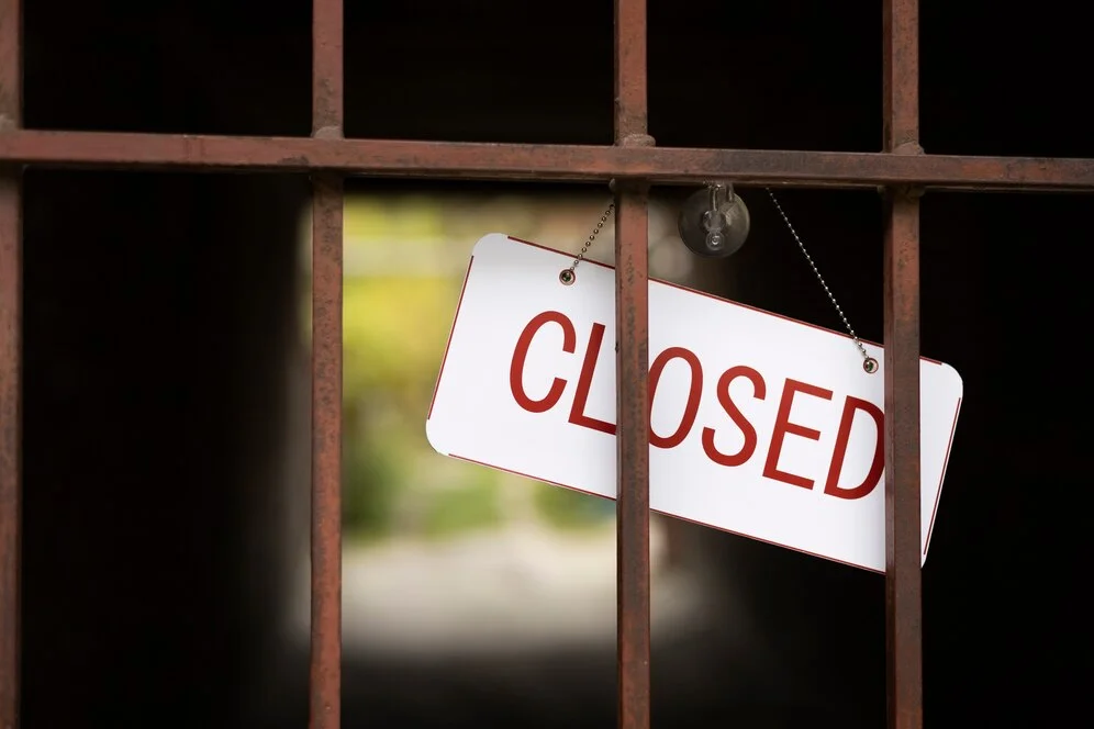 A white "CLOSED" sign hanging behind metal bars, symbolizing a restaurant’s permanent shutdown.